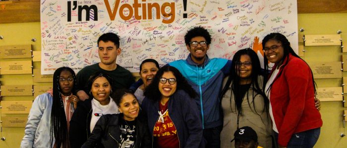 Students of color gather around a signed poster that reads: I'm Voting!
